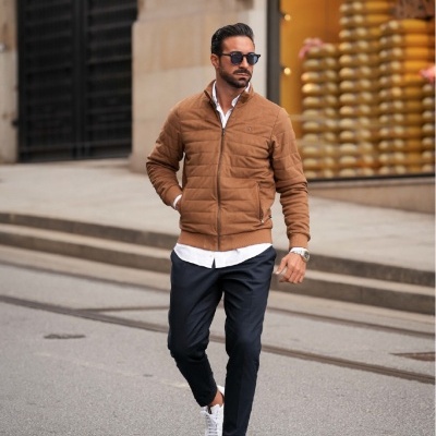 Homem com casaco acolchoado castanho a caminhar numa rua com loja ao fundo