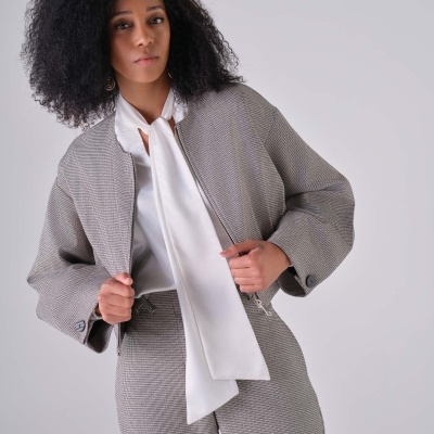 Mulher com conjunto cinzento texturizado e blusa branca num fundo cinza claro
