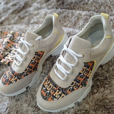 Ténis desportivos bege com tecido estampado e atacadores brancos sobre tapete cinzento.