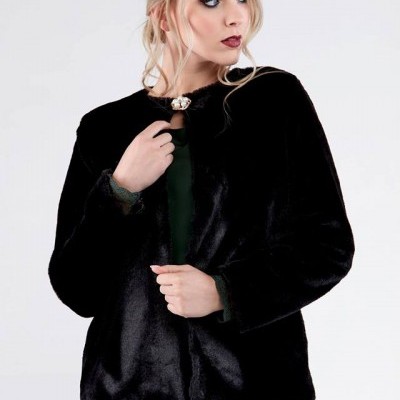 Mulher a usar casaco preto com fecho decorativo na gola e vestido verde por baixo