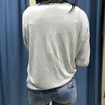 Pessoa de costas com camisola bege e calças de ganga azul claro com bordado floral.