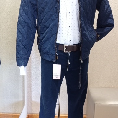 Manequim vestido com roupa casual composta por jaqueta azul almofadada, camisa branca com padrão e calças escuras