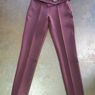 Calças bordô com cintura dobrada e botão prateado sobre chão cinzento