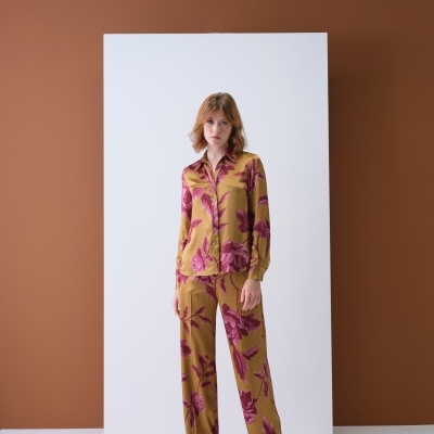 Mulher com conjunto de roupa floral mostarda e borgonha em fundo branco e castanho