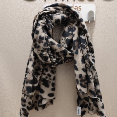 Cachecol com padrão animal print em bege, preto e castanho pendurado em cabide branco