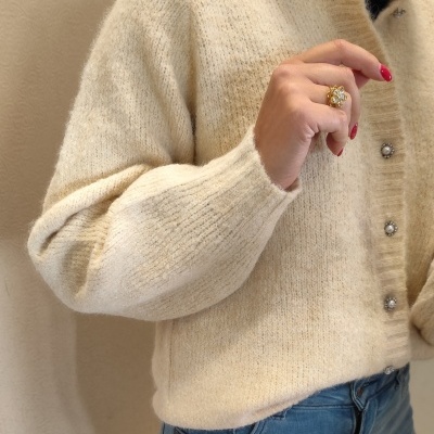 Casaco de malha creme com botões pérola e anel dourado floral.