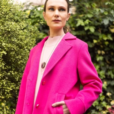 Casaco feminino rosa vibrante com botões, combinado com camisola rosa clara e pendente, ao ar livre com folhagem verde