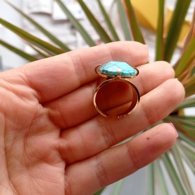 Anel com pedra azul turquesa em mão com folhas ao fundo