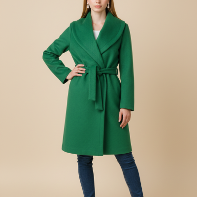 Mulher a vestir casaco verde com cinto, calças de ganga azuis e ténis brancos sobre fundo bege.