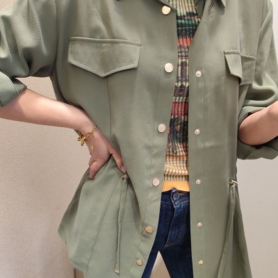 Casaco verde-oliva com botões dourados e bolso, usado com camisola colorida e jeans azul