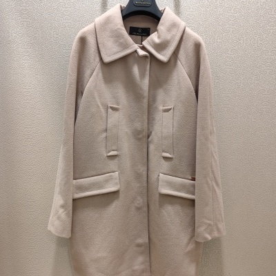 Casaco bege em tecido grosso pendurado na parede com padrão texturizado.