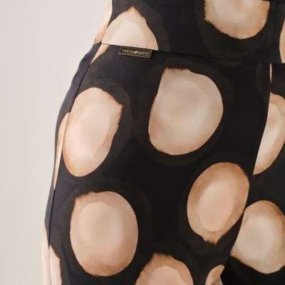 Calças pretas com padrão de círculos castanhos e bege e etiqueta metálica dourada