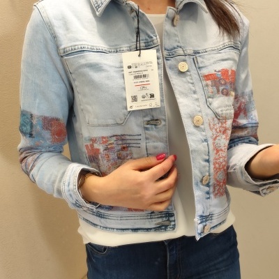 Casaco de ganga azul claro com estampas em vermelho e azul e etiqueta pendurada