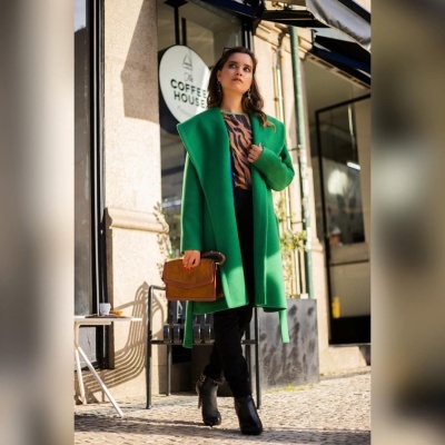 Mulher com casaco verde e camisa animal print perto de um café