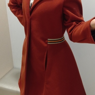 Casaco feminino cor tijolo com gola de lapela e bolsos, em ambiente interior