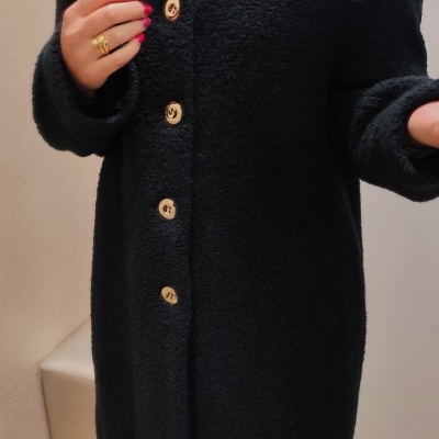 Casaco preto de tecido bouclé com botões dourados e pessoa a usá-lo