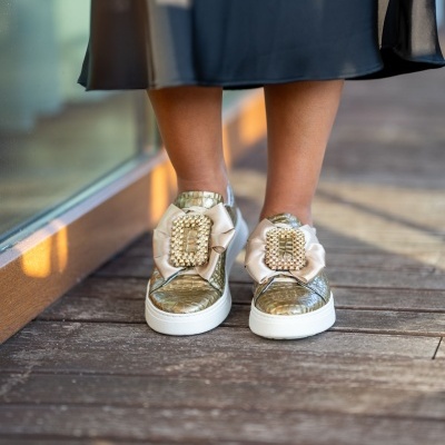 Ténis dourados com detalhes brancos e pérolas usados por mulher com saia preta