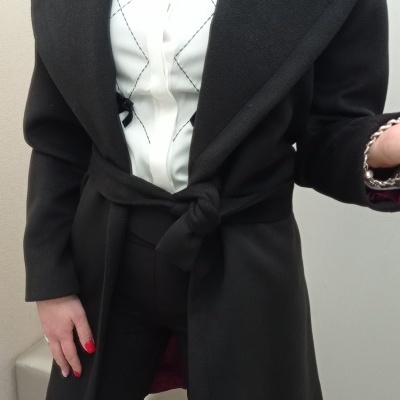 Casaco preto com cinto sobre camisa branca com padrão de linhas diagonais pretas.