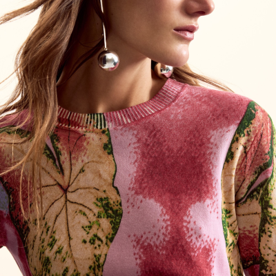 Camisola de malha com padrão de folhas em tons rosa e bege usada por mulher com brincos metálicos grandes