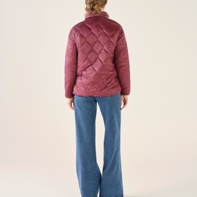 Mulher de costas com casaco acolchoado vinhoso e calças de ganga largas azuis