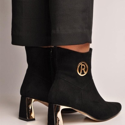 Botins pretos com salto dourado e logo dourado em fundo neutro