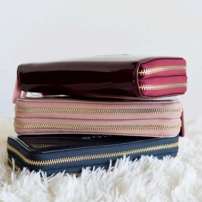 Três carteiras empilhadas em diferentes cores com fechos dourados sobre superfície felpuda branca.