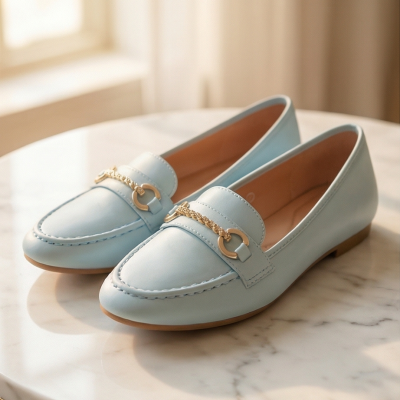 Par de mocassins azuis claros com corrente dourada em mesa de mármore