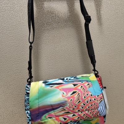 Mala tiracolo colorida com padrão abstracto e alça preta suspensa em fundo decorado.