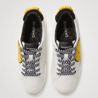 Ténis brancos com detalhes amarelos e atacadores com padrão preto e branco