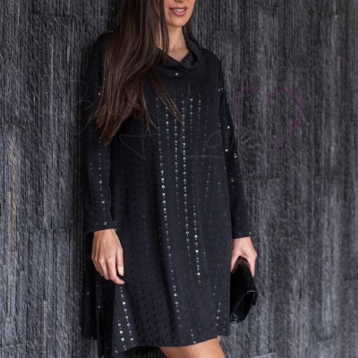 Vestido preto com lantejoulas verticais usado por mulher com botas pretas junto a parede cinza