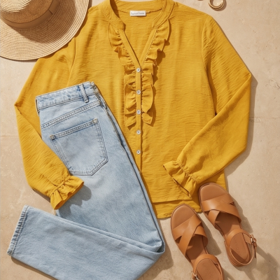 Conjunto de roupa com camisa amarela, calças de ganga, chapéu de palha, brincos dourados e sandálias castanhas