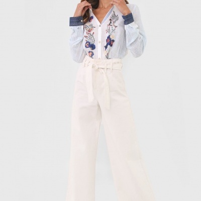 Modelo a usar camisa branca bordada e calças largas brancas com cinto