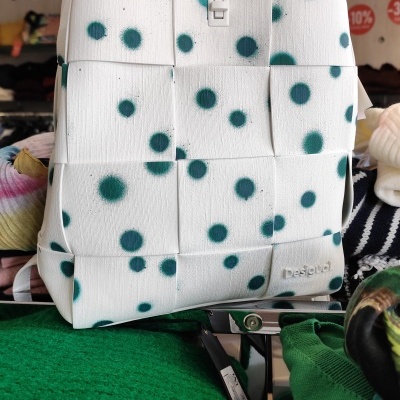 mochila branca com pontos verdes e padrão trançado em exposição