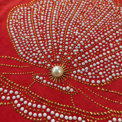 Tecido vermelho com concha decorativa de pontos brancos, dourados e pérola central.