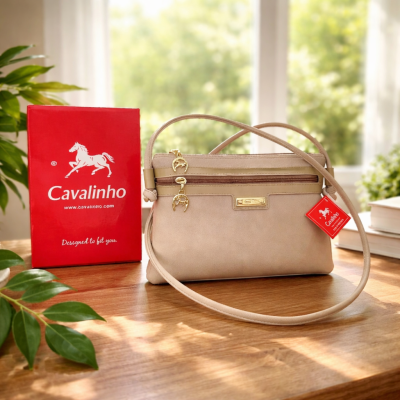 Bolsa bege Cavalinho com fechos dourados e caixa vermelha em mesa de madeira