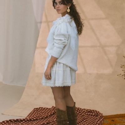 Mulher de perfil com vestido branco, camisola branca felpuda e botas castanhas