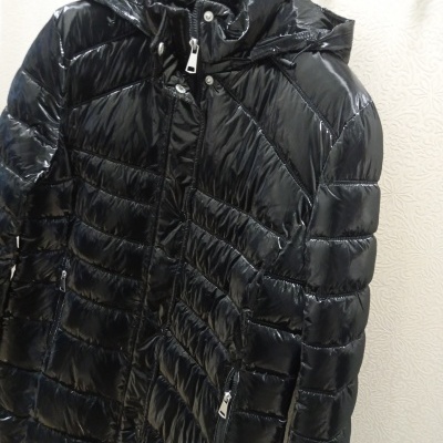 Casaco acolchoado preto brilhante com fecho e capuz pendurado num cabide