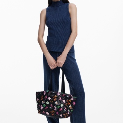 Mulher com conjunto de malha azul escuro e mala de mão preta floral