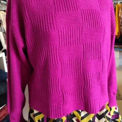 Camisola rosa com padrão quadriculado por cima de camisa com padrão geométrico colorido.