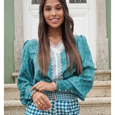 Mulher com blusa azul de padrão hexagonal e roupas azuis com padrão pied-de-poule em escadaria junto a uma porta branca.