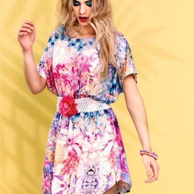 Vestido curto floral colorido com cinto branco e flor rosa, mulher loira, fundo amarelo