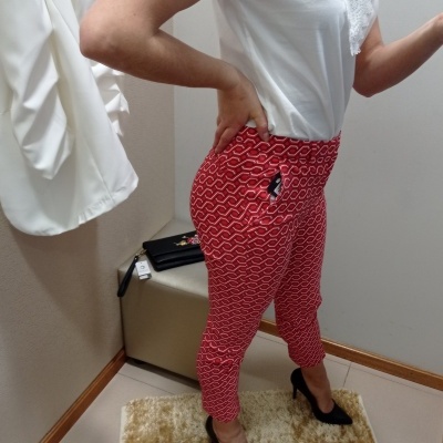 Calças vermelhas com padrão branco e camisa branca, sapatos pretos de salto, em ambiente interior