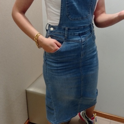Vestido jardineira de ganga azul médio sobre t-shirt branca, com ténis coloridos e pulseira dourada