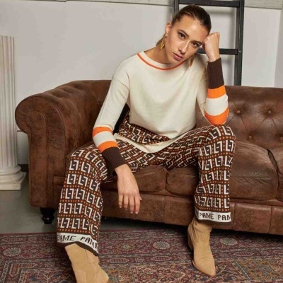 Mulher sentada num sofá castanho com roupa colorida e botas beges