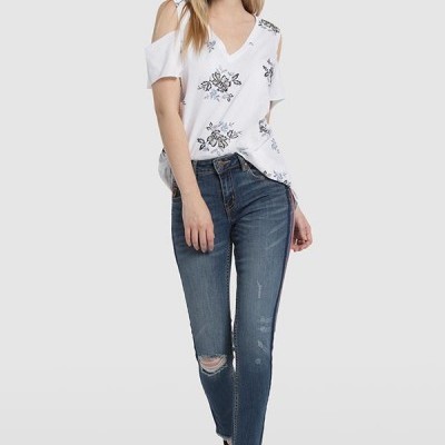 Mulher vestindo camisola branca com flores e jeans azul rasgado com sandálias pretas.