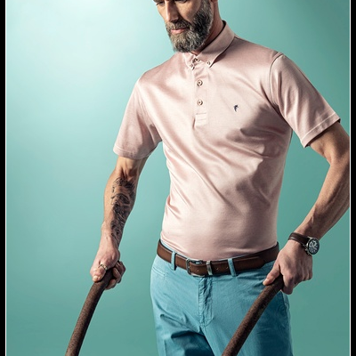 Homem com polo rosa e calças azuis a empurrar carrinho de mão com flores