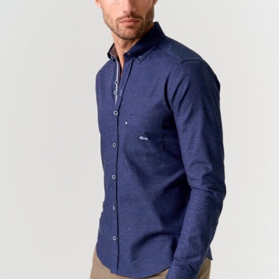 Homem com camisa azul escura de manga comprida e calças bege em fundo branco.