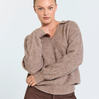 Mulher de cabelo apanhado a usar camisola castanha de malha e calças castanhas