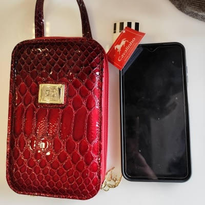 Mala pequena vermelha em verniz com padrão crocodilo e etiqueta Cavalinho ao lado de smartphone preto