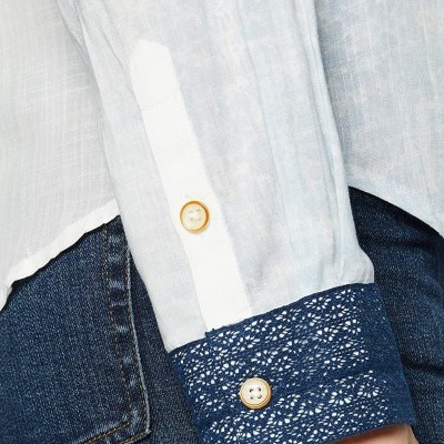 Manga de camisa branca com punho em renda azul e botão, com calças de ganga